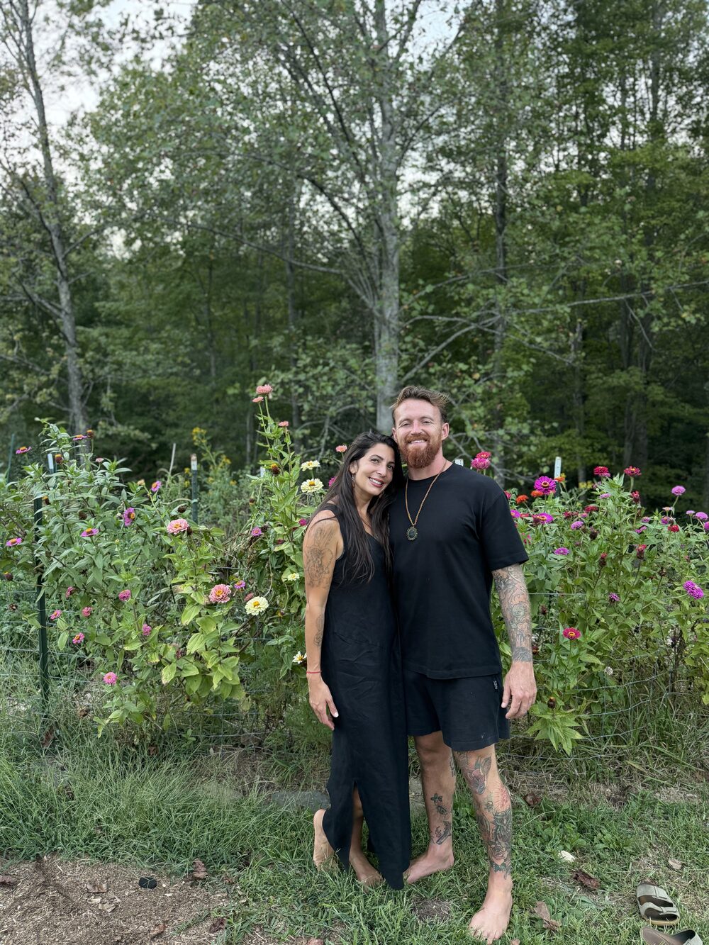 Ste and his partner standing barefoot in front of a flower garden